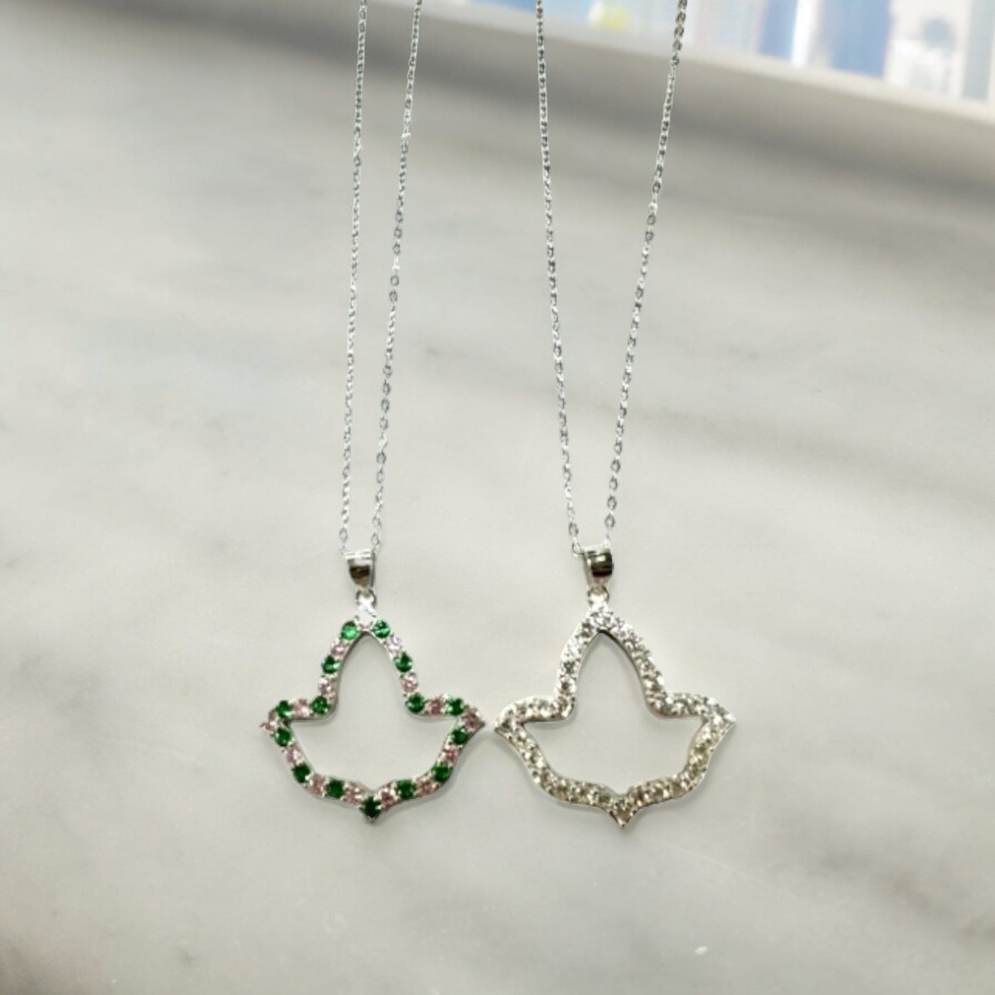 Elegant AKA Open Ivy Leaf Necklaces with sparkling pink and green, and clear cubic zirconia diamonds, crafted from high-quality .925 sterling silver with rhodium plating, showcased on a light gray surface.