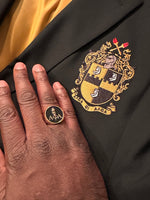 Alpha Phi Alpha Light of the World Gold Ring worn on a hand, displayed against a jacket with the Alpha Phi Alpha fraternity crest.