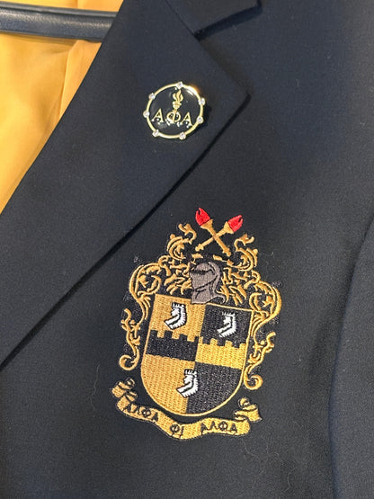 Gold-plated Alpha Phi Alpha Light Of The World lapel pin with seven diamonds on a black blazer featuring the fraternity's embroidered crest.