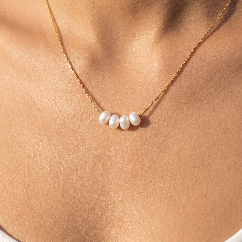Dainty gold pearl necklace worn at the collarbone