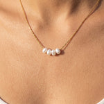 Dainty gold pearl necklace worn at the collarbone
