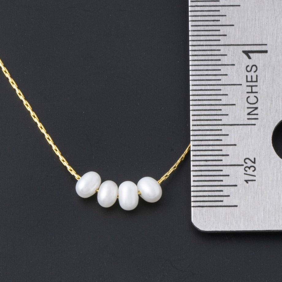 Dainty gold glass pearl necklace next to a ruler showing the pearl size