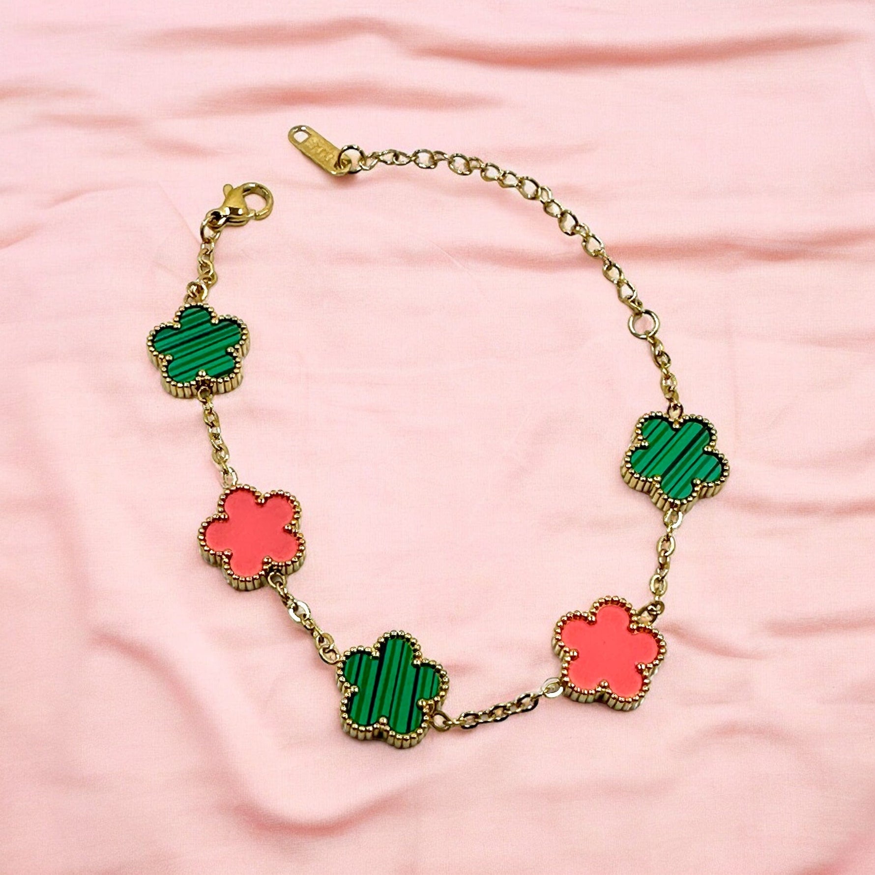 Stylish Kaitlin Flower Clover bracelet with pink and green clover-shaped charms, crafted in gold-plated stainless steel, displayed on a light pink fabric background.