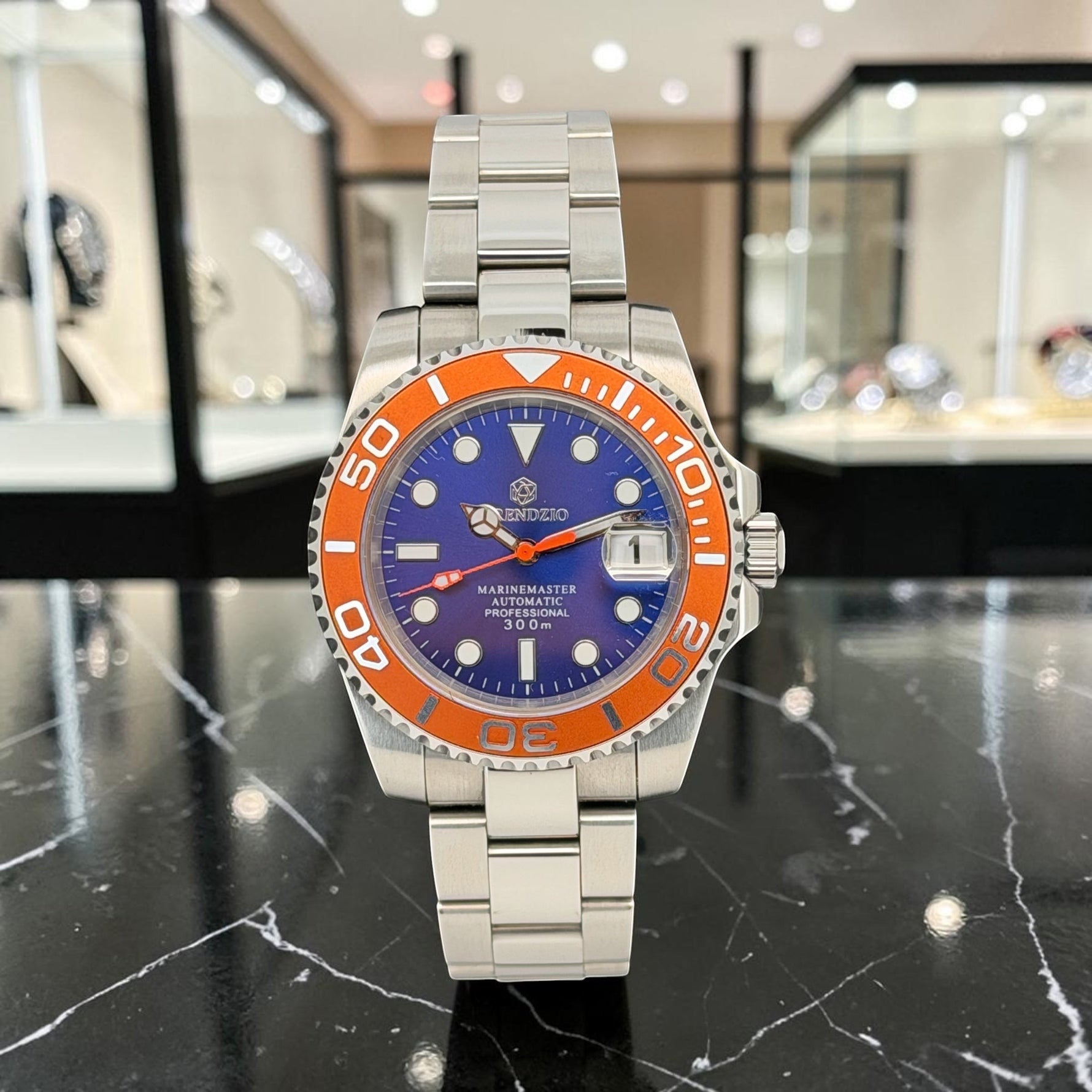 Trendzio Jewelry Blue Amber Mariner automatic watch with orange bezel, blue dial, stainless steel bracelet, and date window.