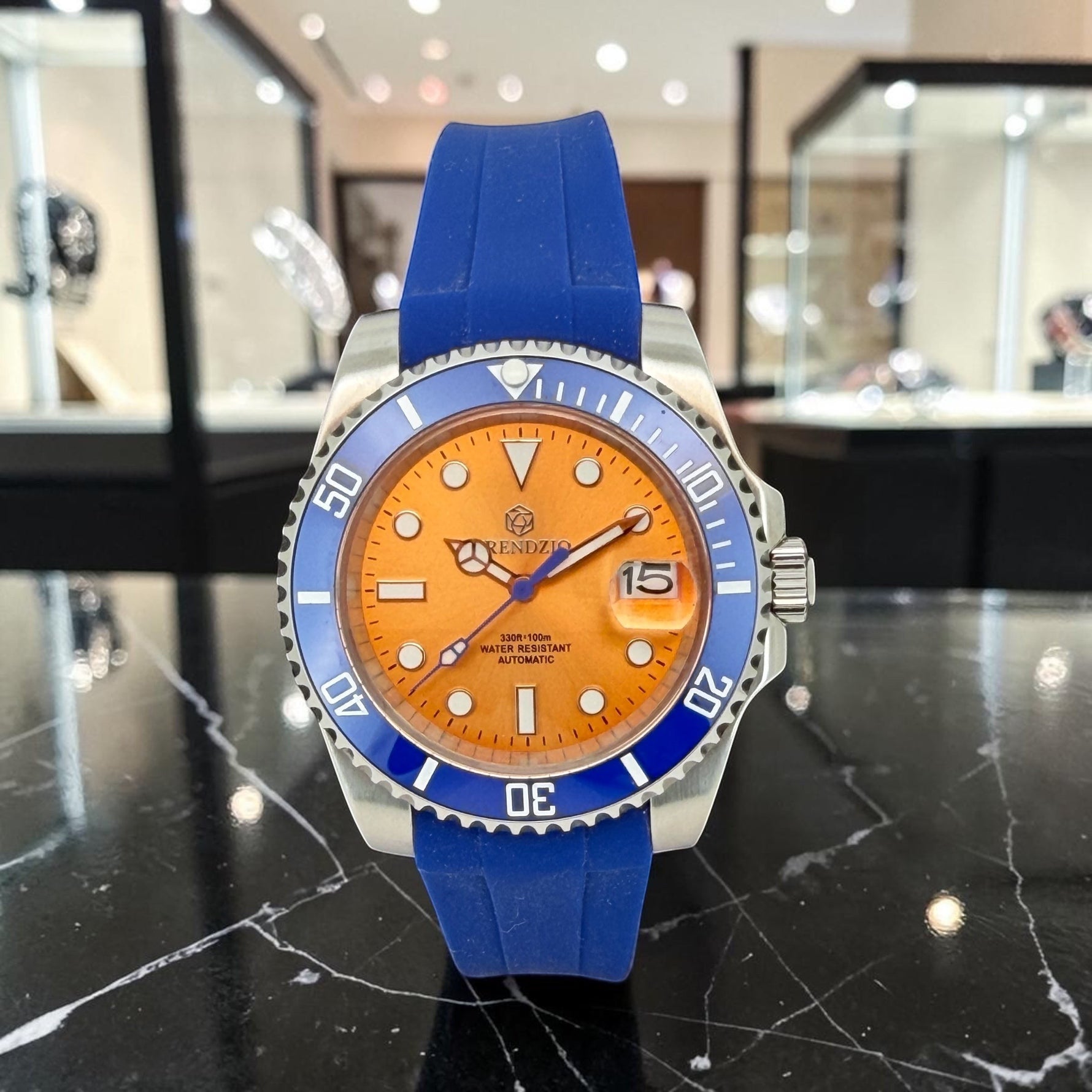 Trendzio Jewelry Blue Amber automatic watch with orange dial, blue bezel, and blue rubber strap. Features date window and luminous markers.