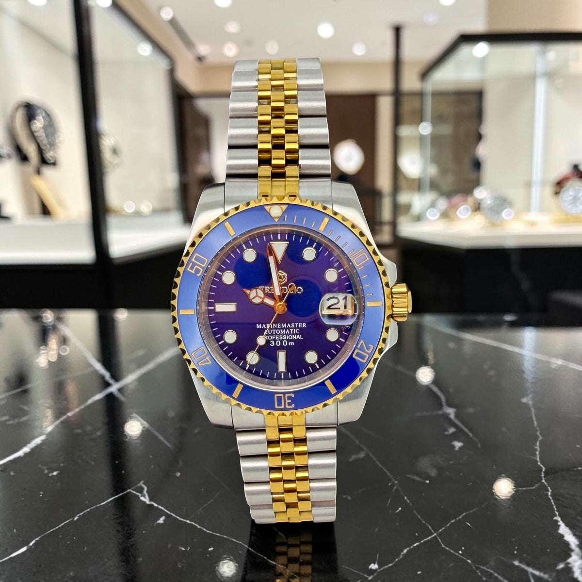 Trendzio Jewelry Blue Oro Mariner watch with sunburst blue dial, gold hands, and blue ceramic bezel. Stainless steel bracelet.