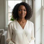 Woman wearing a Trendzio Jewelry gold Delta Sigma Theta Greek letter necklace with a white blouse by a window.