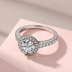 Trendzio Jewelry Lyra sterling silver ring featuring a round halo CZ diamond on a pavé band against a pink backdrop.