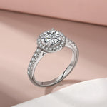 Trendzio Jewelry Lyra sterling silver ring with a round halo CZ diamond and pavé band on a soft pink background.