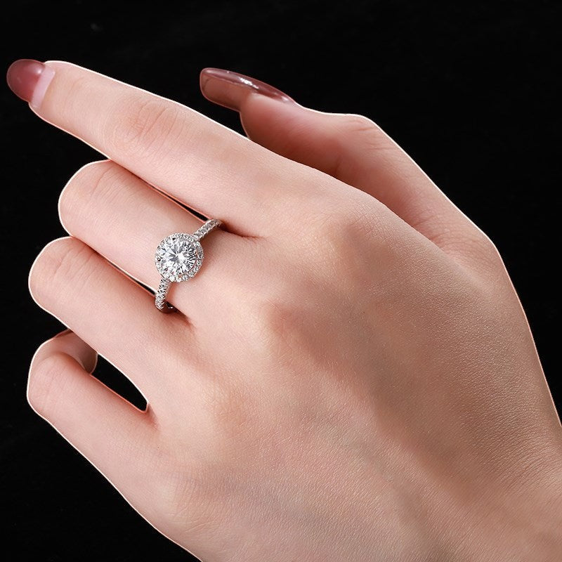 Trendzio Jewelry Lyra sterling silver ring with a round halo CZ diamond on a woman's finger against black background